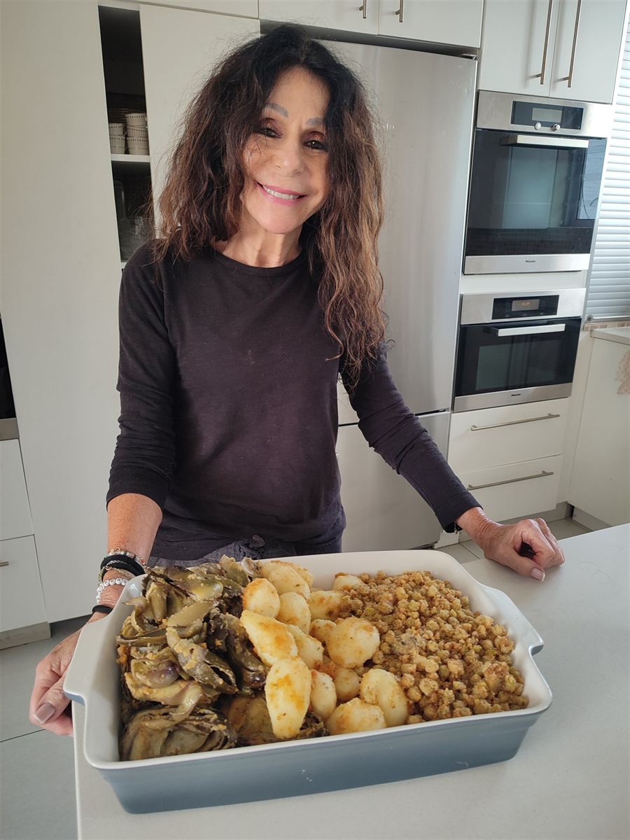 Sheila in her kitchen holding a dish of artichokes and potatoes